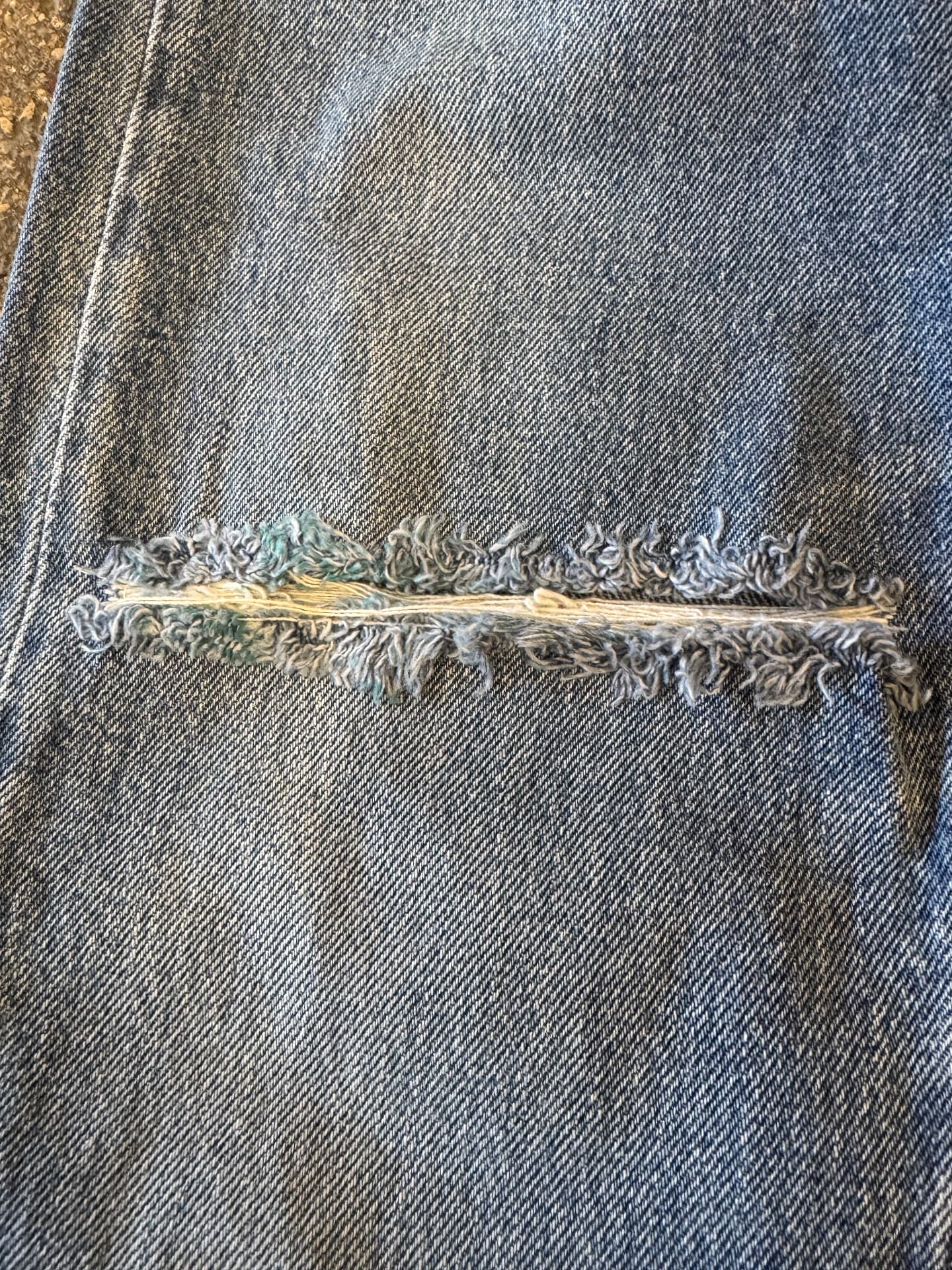 Gros plan sur une déchirure de denim vintage patiné et ses fils effilochés